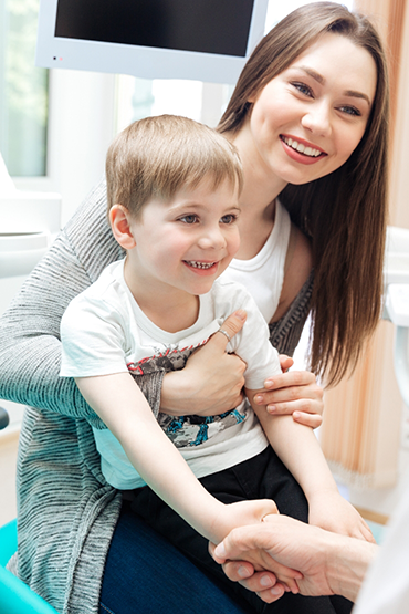 Young boy shaking hands with his dentist while sitting in his mothers lap